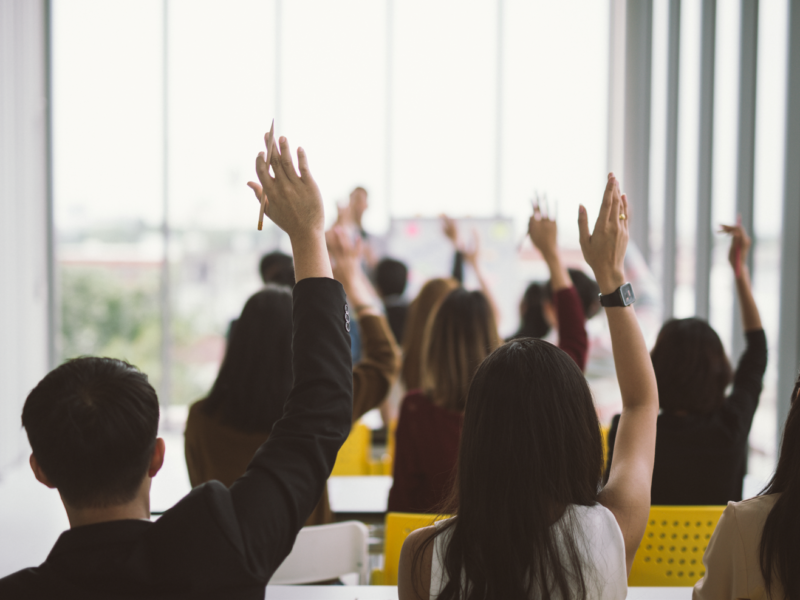 A back view of a group of people with their hands raised. | Vue arrière d'un groupe de personnes aux mains levées.